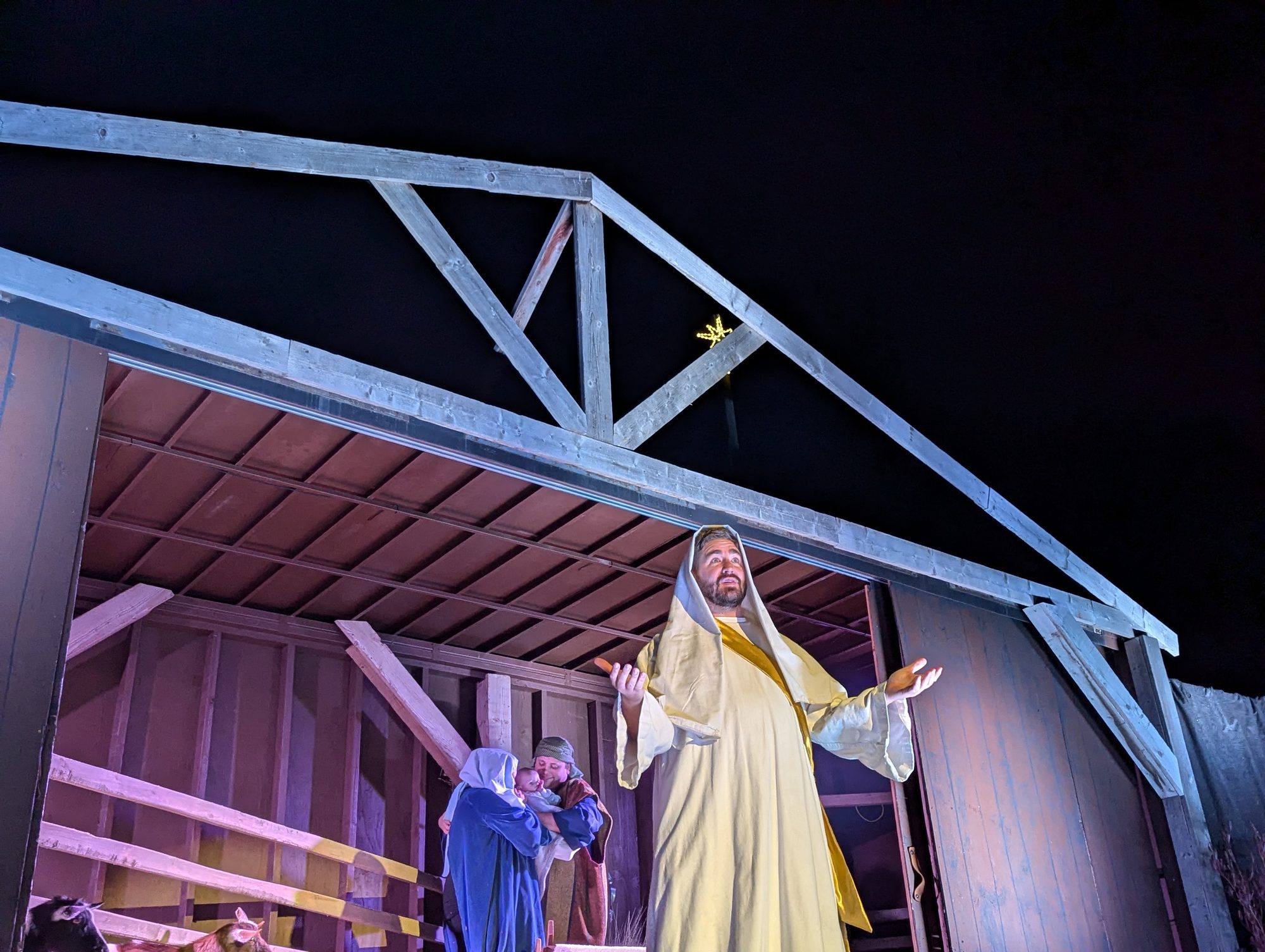 Costumed actor portraying Jesus speaking beside Mary and Joseph in the nativity stable